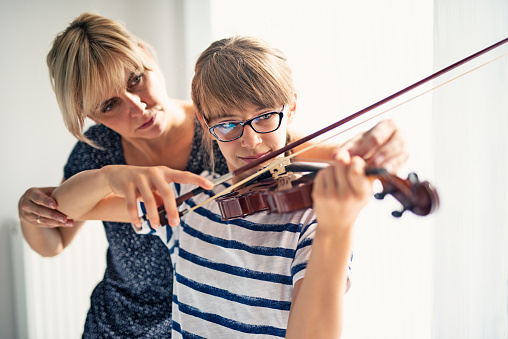 Teenage girl aged 10 is practicing violin. Mother is helping her by correcting her posture. Both are having fun during the lesson.